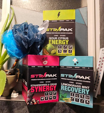STiiMPAK Shower Steamer boxes stacked on top of each other. Synergy, Recovery, and Energy. With a loofah