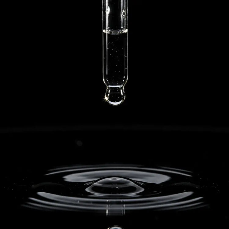 Dropper with clear liquid above a black surface creating ripples.