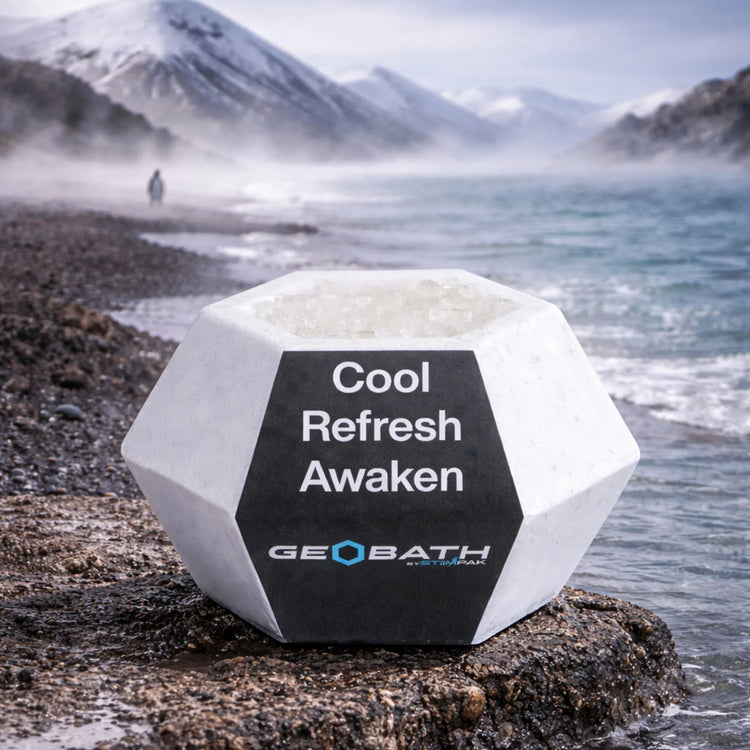 Geobath Geode Bath Bomb with 'Cool Refresh Awaken' text on a rocky shore with water and mountains in the background