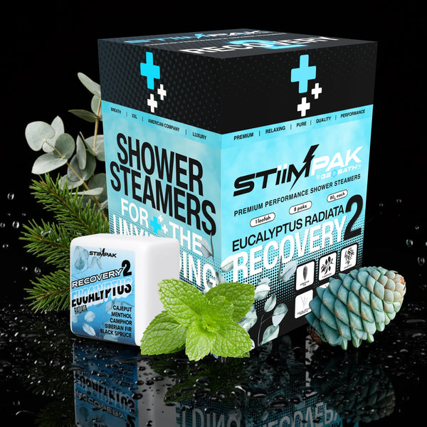 STIMPAK Shower Steamers Recovery 2 box and single sachet displayed with eucalyptus leaves, mint leaves, and a pine cone on a glossy black reflective surface.