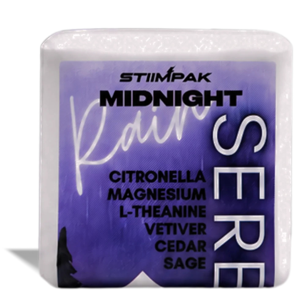 A shower steamer cube featuring a purple label with the brand STIIMPAK and scent name Midnight Rain, plus listed ingredients including citronella, magnesium, L-theanine, vetiver, cedar, and sage.
