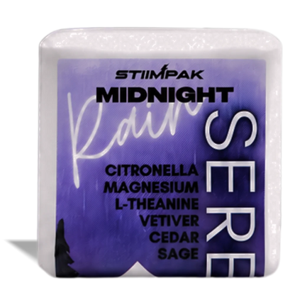 A shower steamer cube featuring a purple label with the brand STIIMPAK and scent name Midnight Rain, plus listed ingredients including citronella, magnesium, L-theanine, vetiver, cedar, and sage.